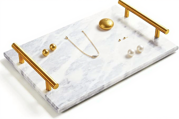 Marble tray with gold handles holding jewelry on a white background